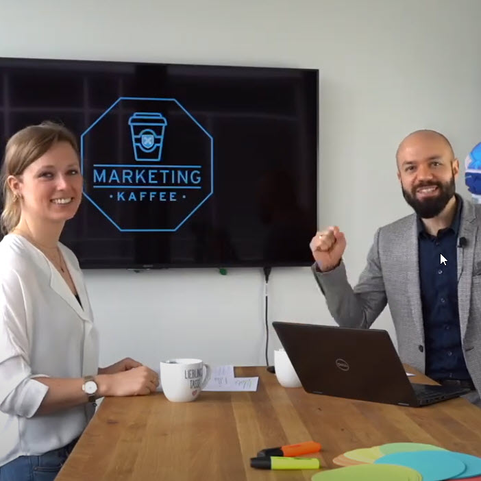 Zwei Concordia Mitarbeiter stehen an einem Tisch und arbeiten am Marketing Kaffee Konzept.