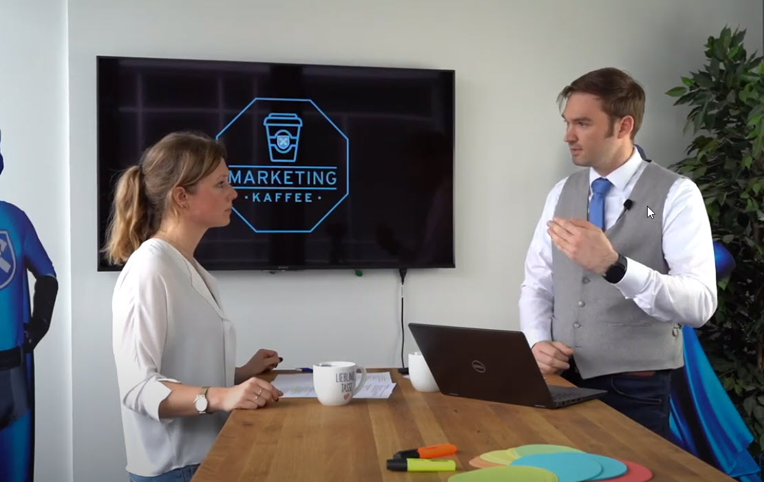 Zwei Concordia Mitarbeiter stehen an einem Tisch und arbeiten am Marketing Kaffee Konzept.